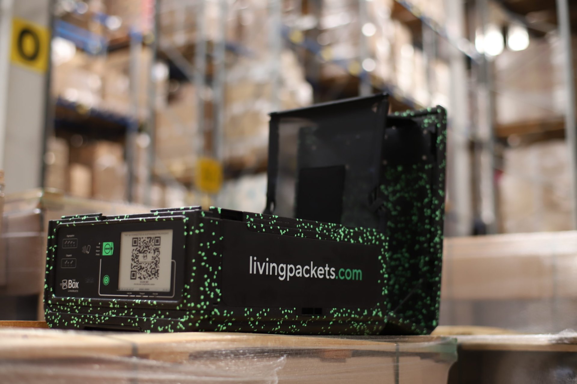 LivingPackets THE BOX smart reusable parcel on a pallet in a warehouse, showing the e-ink label and QR code